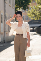 a lady in a beige top, a white openwork jacket and a pair of brown pants